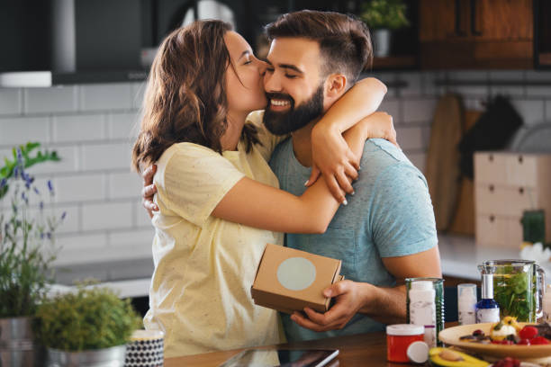 Young couple in the kitchen. The man surprised his girlfriend with an unexpected gift. She is happy. Hugging him and kissing.